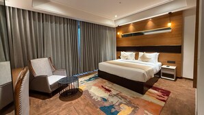 Una habitación de hotel moderna con una cama grande, una silla, una mesita y una alfombra estampada.