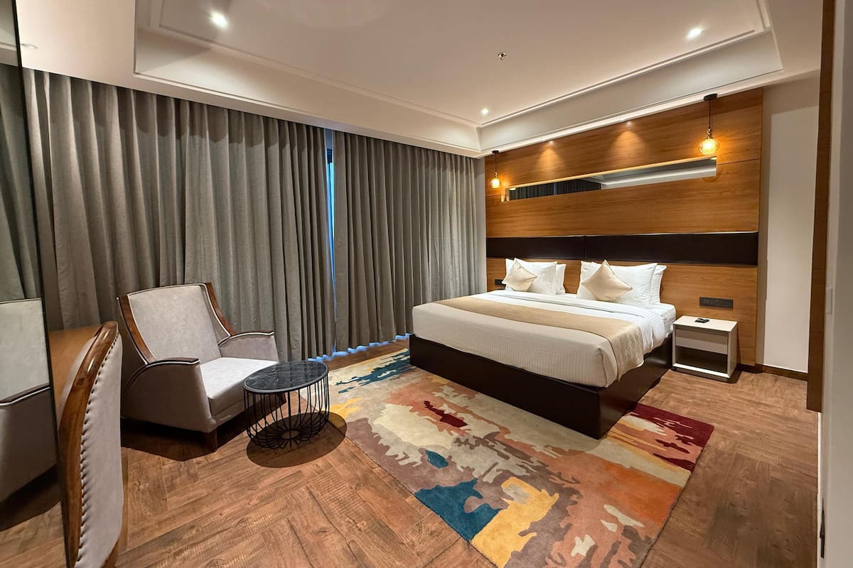Quarto de hotel moderno com uma cama grande, uma cadeira, uma mesa pequena e um tapete estampado.