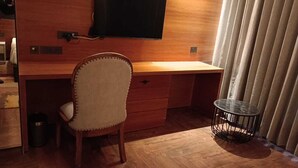Un escritorio de madera con una silla, un televisor montado encima y una mesita redonda con estructura de alambre.