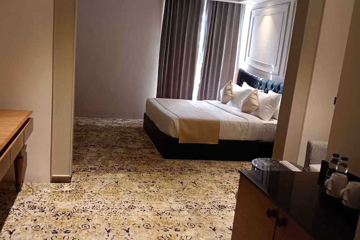 Quarto de hotel com uma cama, um banco de madeira, uma escrivaninha e uma mesa pequena.