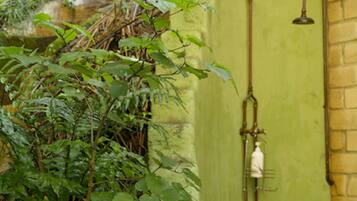 Uma área de chuveiro externo rústica, com parede verde, banco de madeira e muita vegetação.