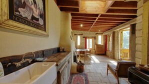 Ein rustikales Interieur mit Holzbalkendecke, einer großen weißen Badewanne, einem Essbereich mit Tisch und Stühlen sowie einem gerahmten Bild an der Wand.