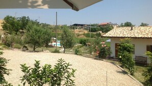 Une vue depuis un balcon donnant sur une cour en gravier, avec des arbres et un petit bâtiment doté d’un toit en tuiles.