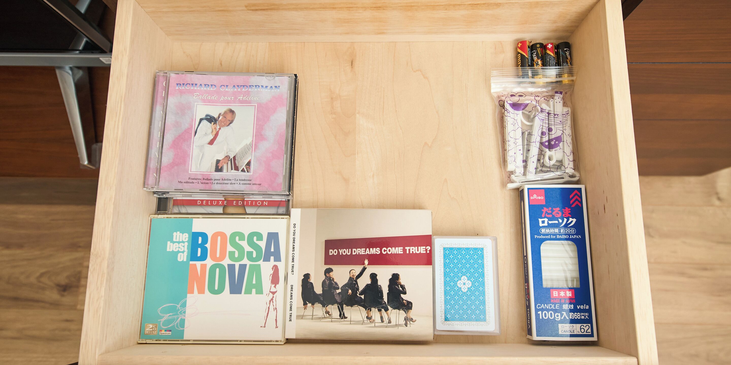 A wooden drawer containing various items including a CD, a book, a candle, and a small box.
