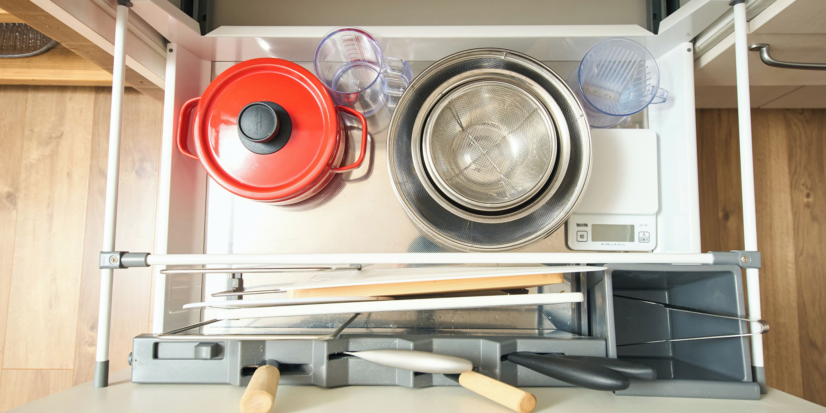 Una cocina con lavavajillas incorporado, una olla roja, un colador y una taza medidora.