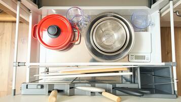 Una cocina con lavavajillas incorporado, una olla roja, un colador y una taza medidora.