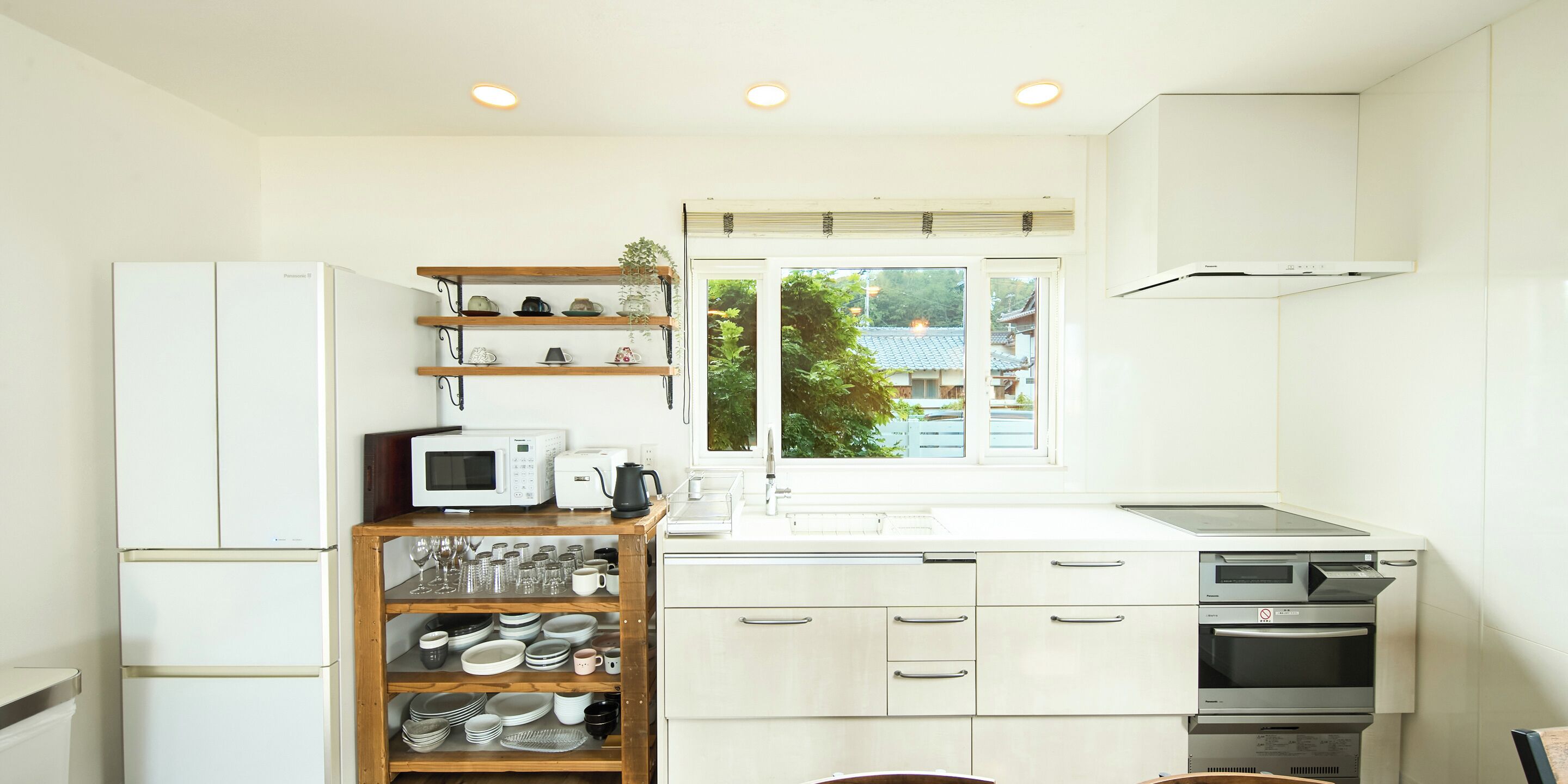 A modern kitchen with white cabinets, a microwave, a toaster, and a coffee maker. There is a window with a view of a tree and buildings outside.