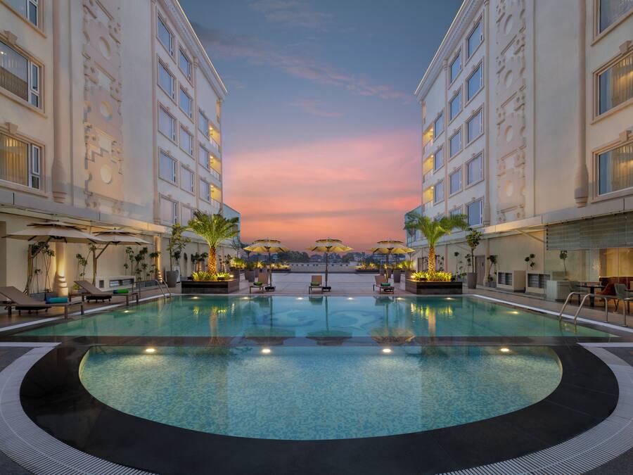 A pool area with lounge chairs and umbrellas, surrounded by buildings with balconies.