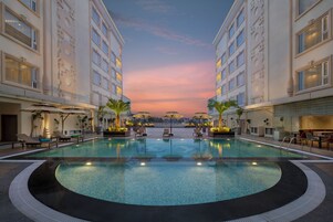 Zona de piscina con sillones de playa y sombrillas, rodeada de edificios con balcones.
