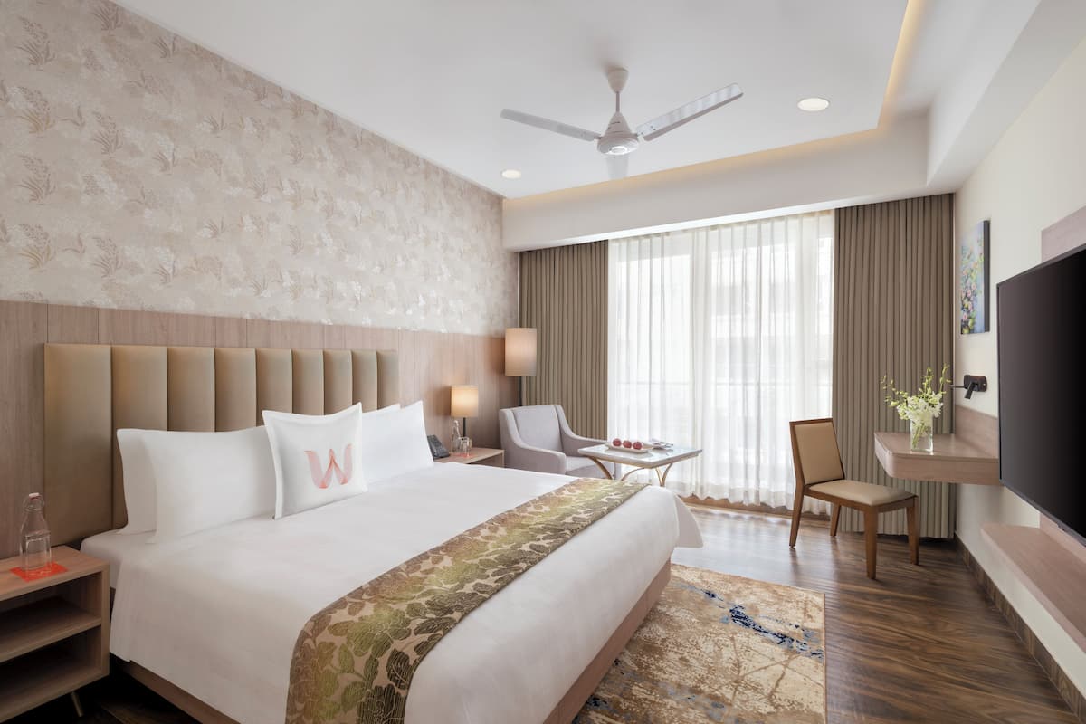 Une chambre d’hôtel avec un grand lit, un bureau avec une chaise, une télévision et un ventilateur de plafond.