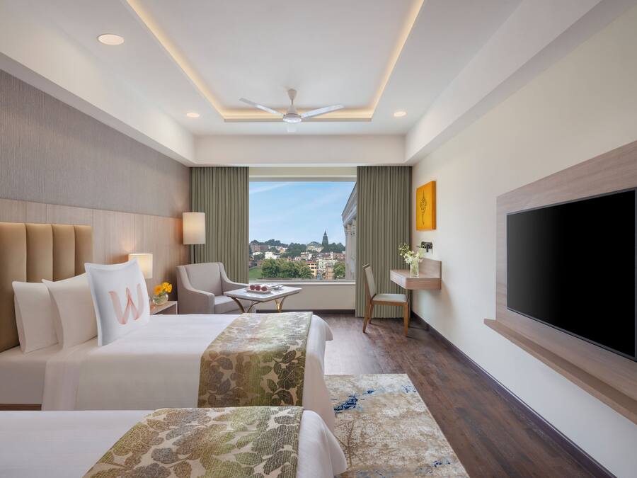 A hotel room with a bed, a desk, a chair, a TV, and a view of the city.