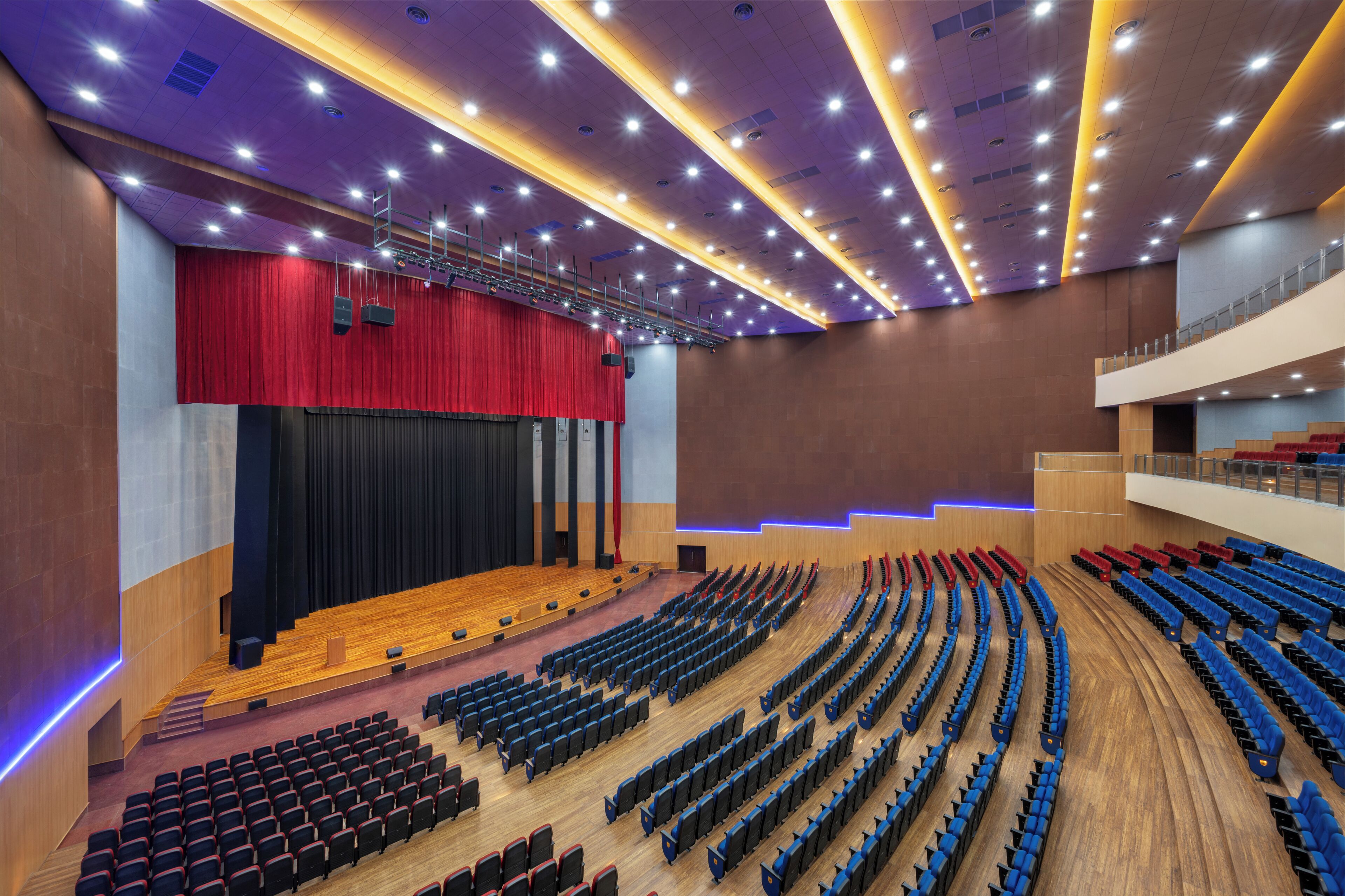 Un auditorio moderno con asientos escalonados, un escenario con cortina roja y suelo de madera.