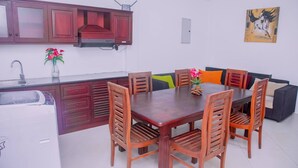 Une cuisine compacte équipée d’un four à micro-ondes, d’un évier et d’un placard. On y trouve une table à manger avec six chaises et un canapé avec des coussins. Un tableau est accroché au mur.