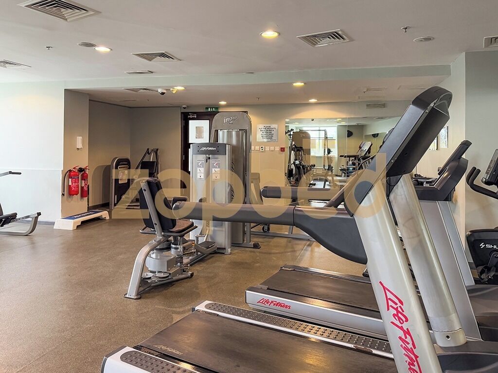 Une salle de sport équipée de tapis de course, d’appareils de musculation et d’un mur recouvert de miroirs.