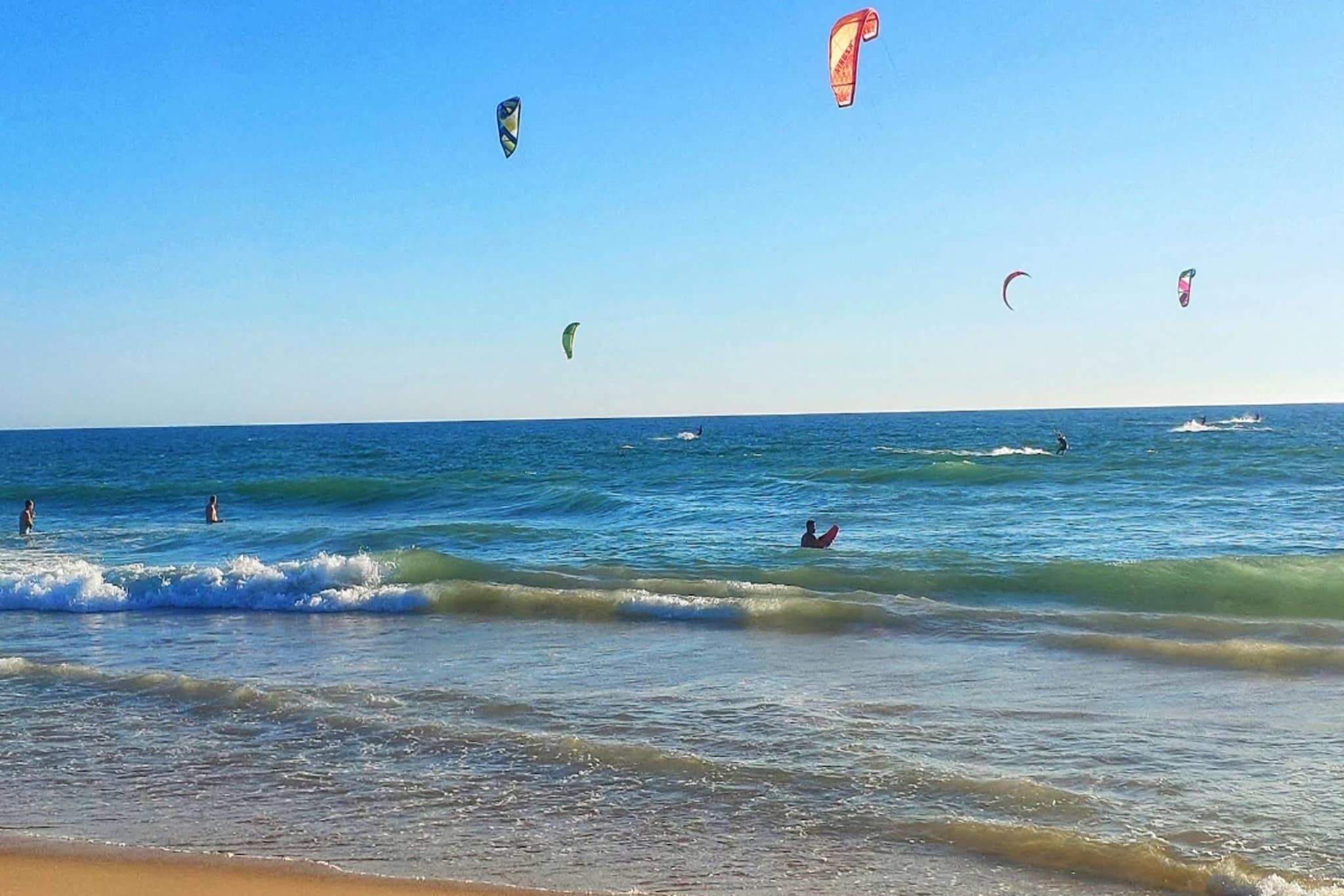 Een strand met heldere lucht en mensen die watersporten beoefenen.