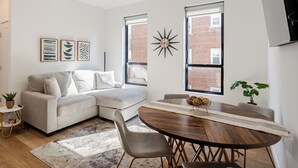 A modern living room with a sofa, a dining table, and a large window.