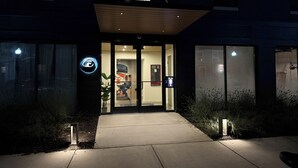 A building entrance with a glass door, a small outdoor area with plants, and a visible sign.
