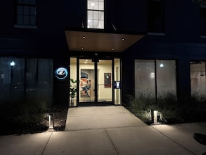 A building entrance with a glass door, a small outdoor area with plants, and a visible sign.