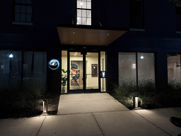 A building entrance with a glass door, a small outdoor area with plants, and a visible sign.