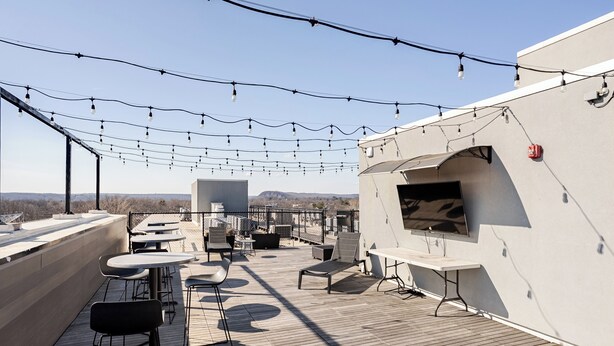 A rooftop terrace with tables, chairs, string lights, and a flat-screen TV.