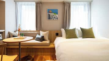 A hotel room with a bed, a sofa, a small table, and a chair. There is a painting on the wall and a window with curtains.