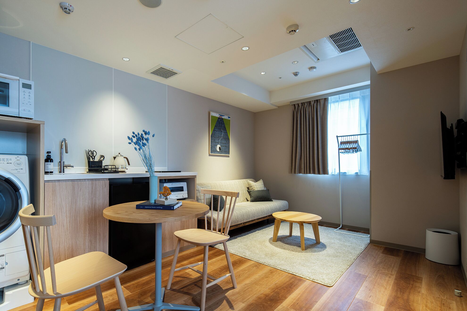 A modern, well-lit room with a kitchen area, a seating area with a sofa and chairs, and a large window with curtains.