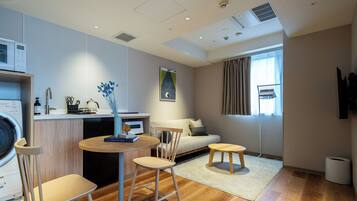 A modern, well-lit room with a kitchen area, a seating area with a sofa and chairs, and a large window with curtains.