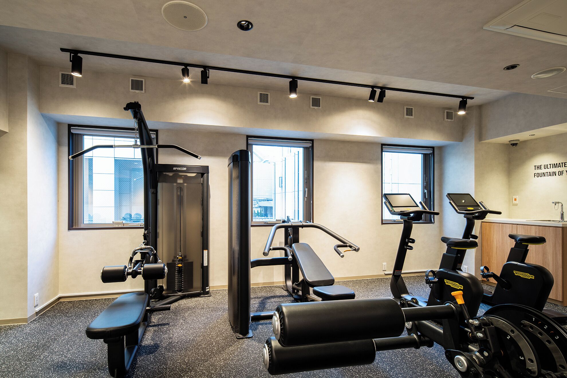 Ein Fitnessstudio mit Trainingsgeräten, großen Fenstern und einer Wand mit Text.