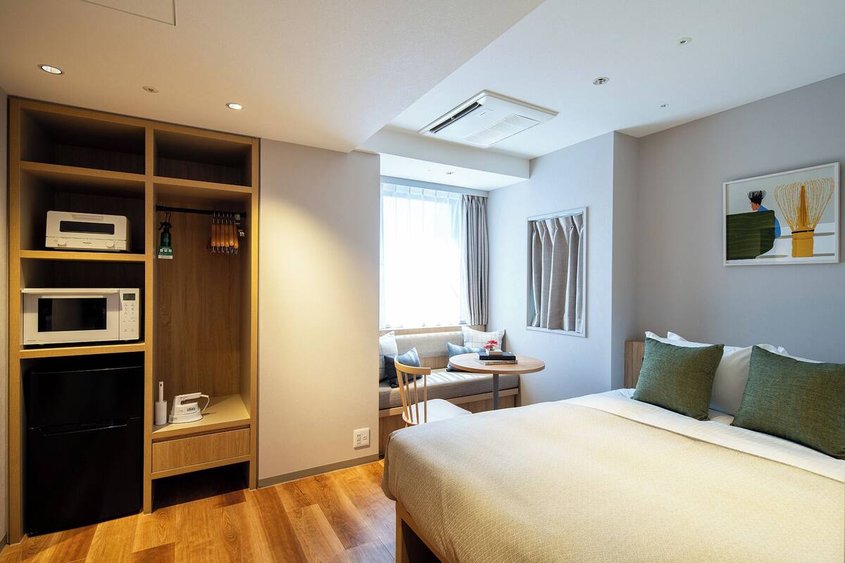 Quarto de hotel com cama, mesa de trabalho, micro-ondas, frigorífico e guarda-roupa.