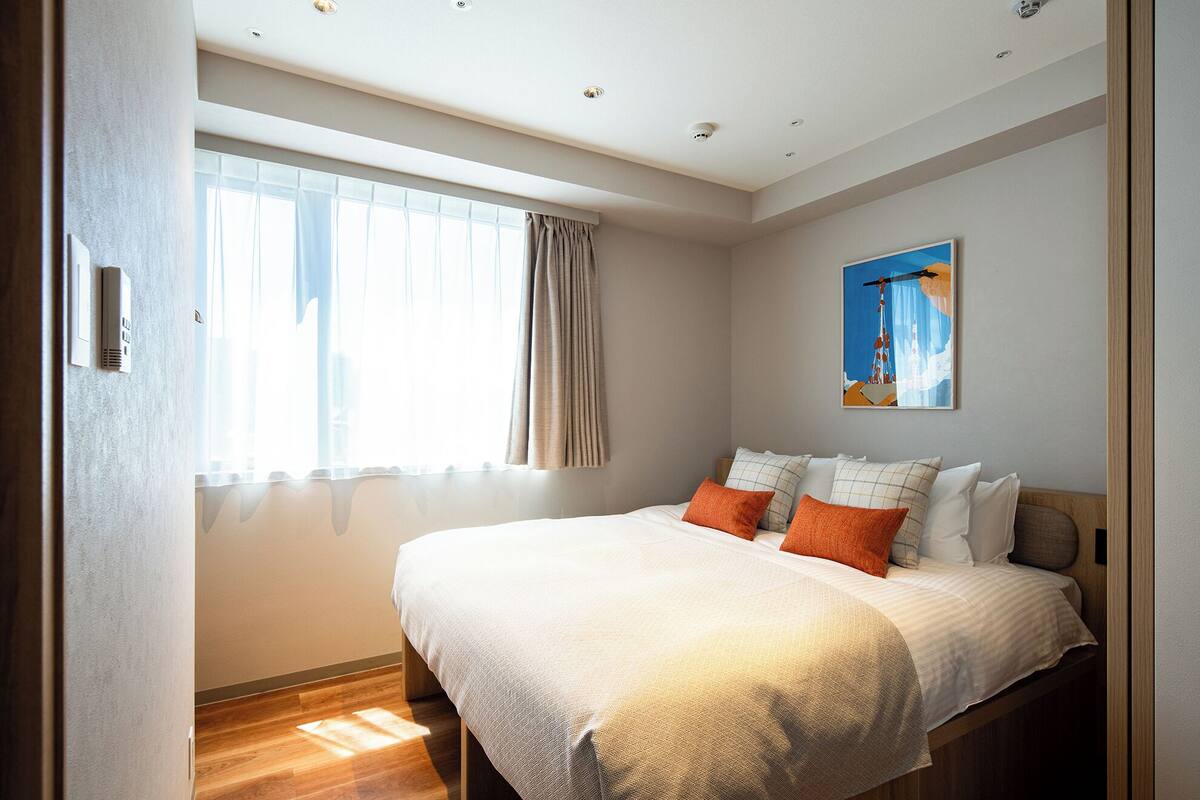 Quarto com cama grande, janela com cortinas, teto com iluminação embutida e um quadro na parede.
