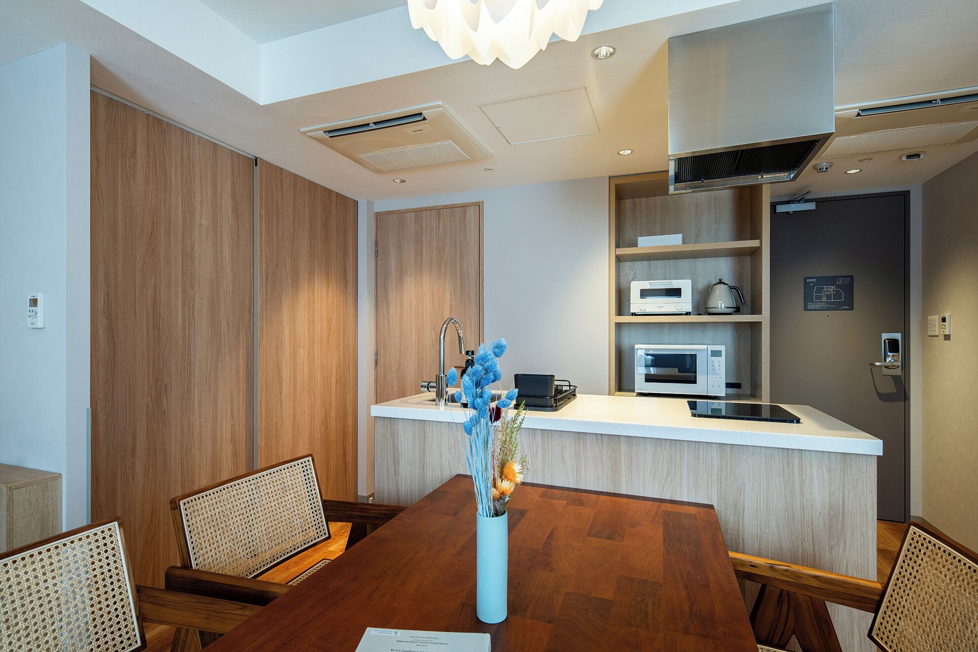 A modern kitchen with built-in appliances, a dining area with a wooden table and chairs, and a decorative vase with blue flowers.