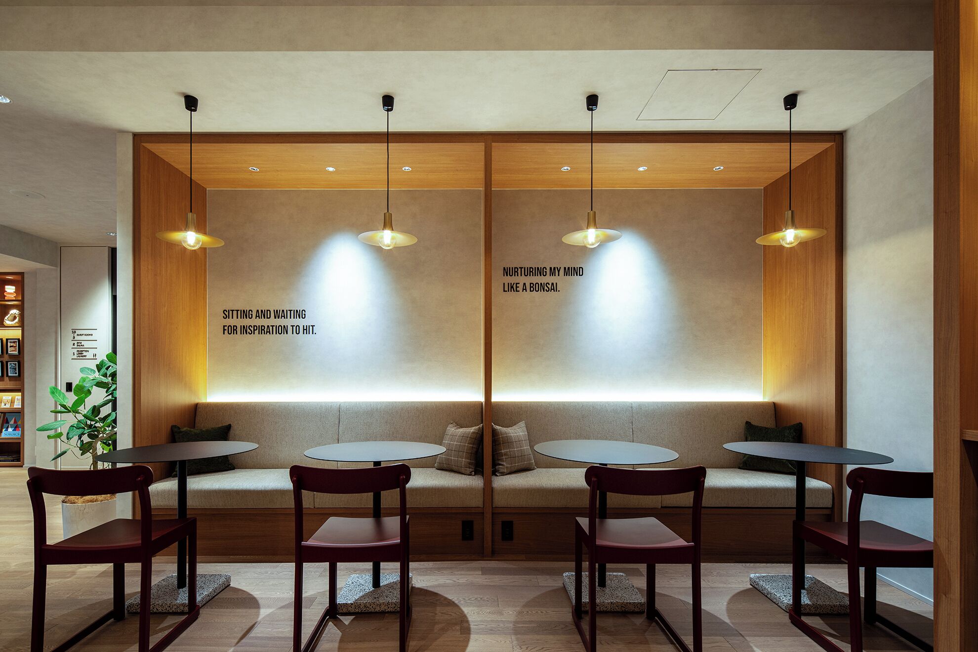 Un interior moderno con una zona de estar que incluye mesas y sillas redondas, separadores de madera e iluminación colgante.