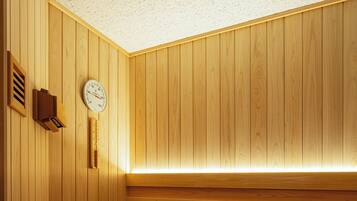 A wooden sauna with a sloped bench, a wall-mounted heater, a clock, and a ventilation vent.