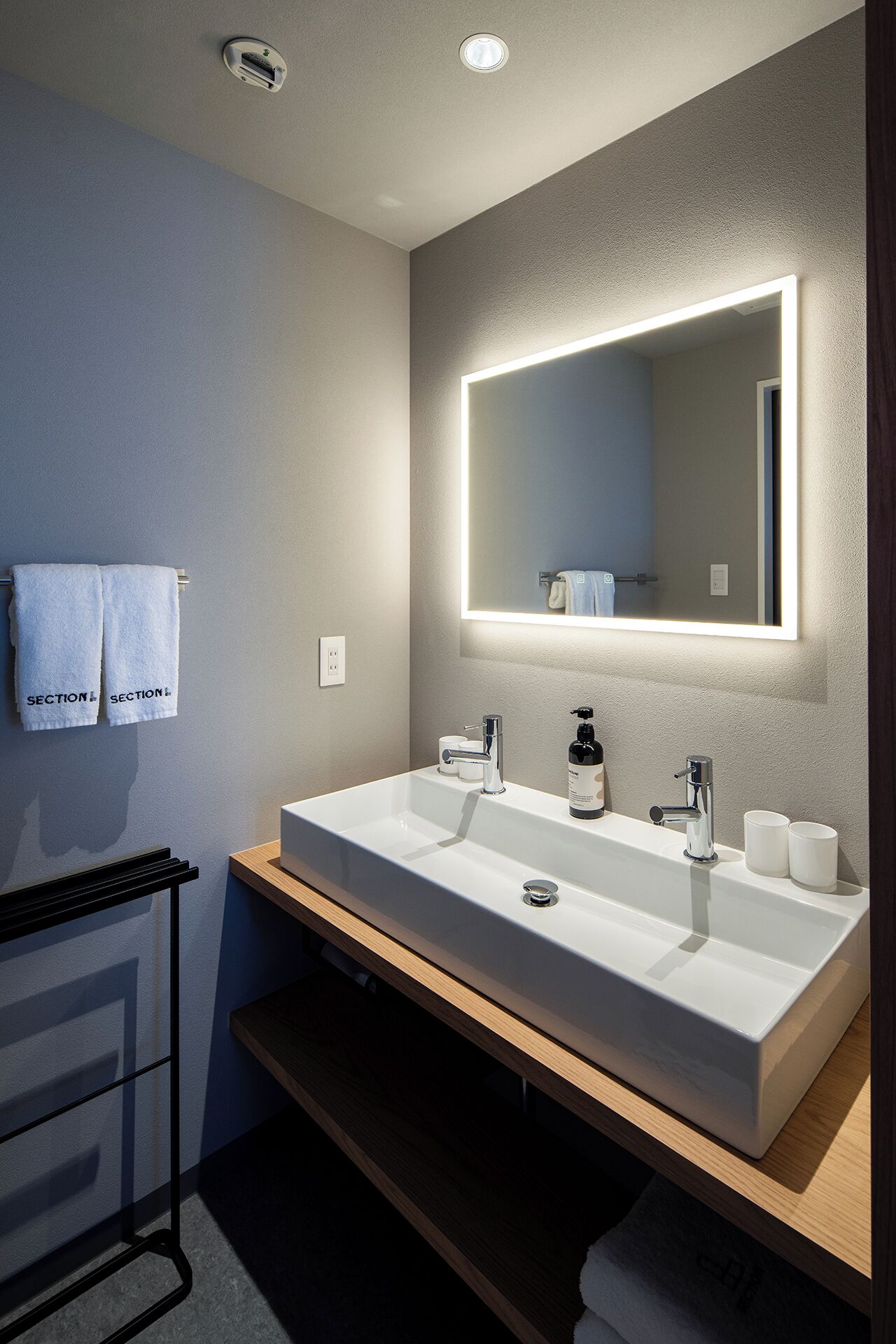 A modern bathroom with a large mirror, two sinks, and a towel rack.