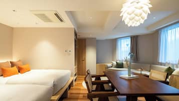 A modern hotel room with a bed, a dining table with chairs, a sofa, and a large window with curtains.