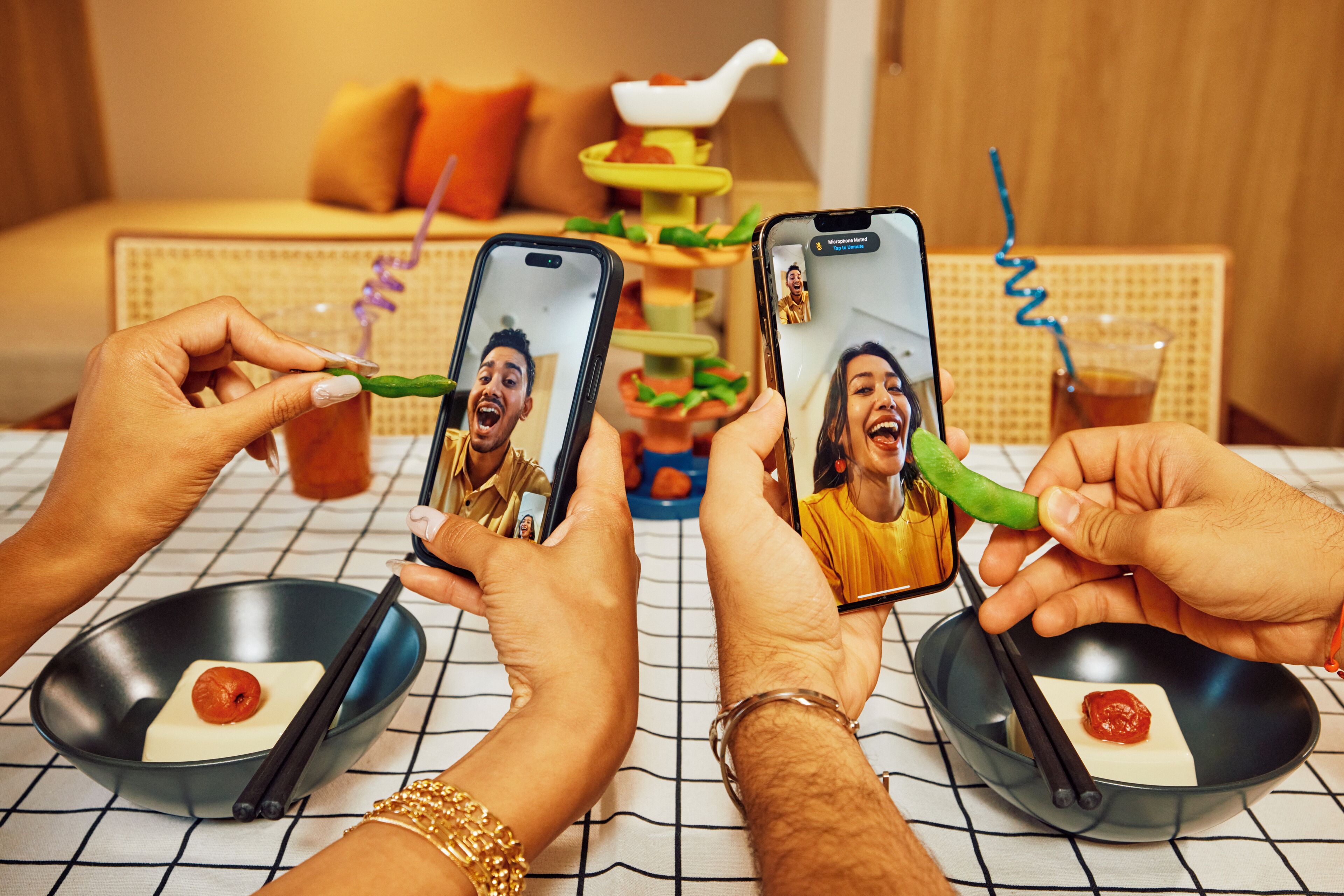 A dining table with two bowls of food, a person holding a smartphone, and another person holding chopsticks.