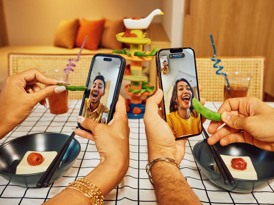 A dining table with two bowls of food, a person holding a smartphone, and another person holding chopsticks.