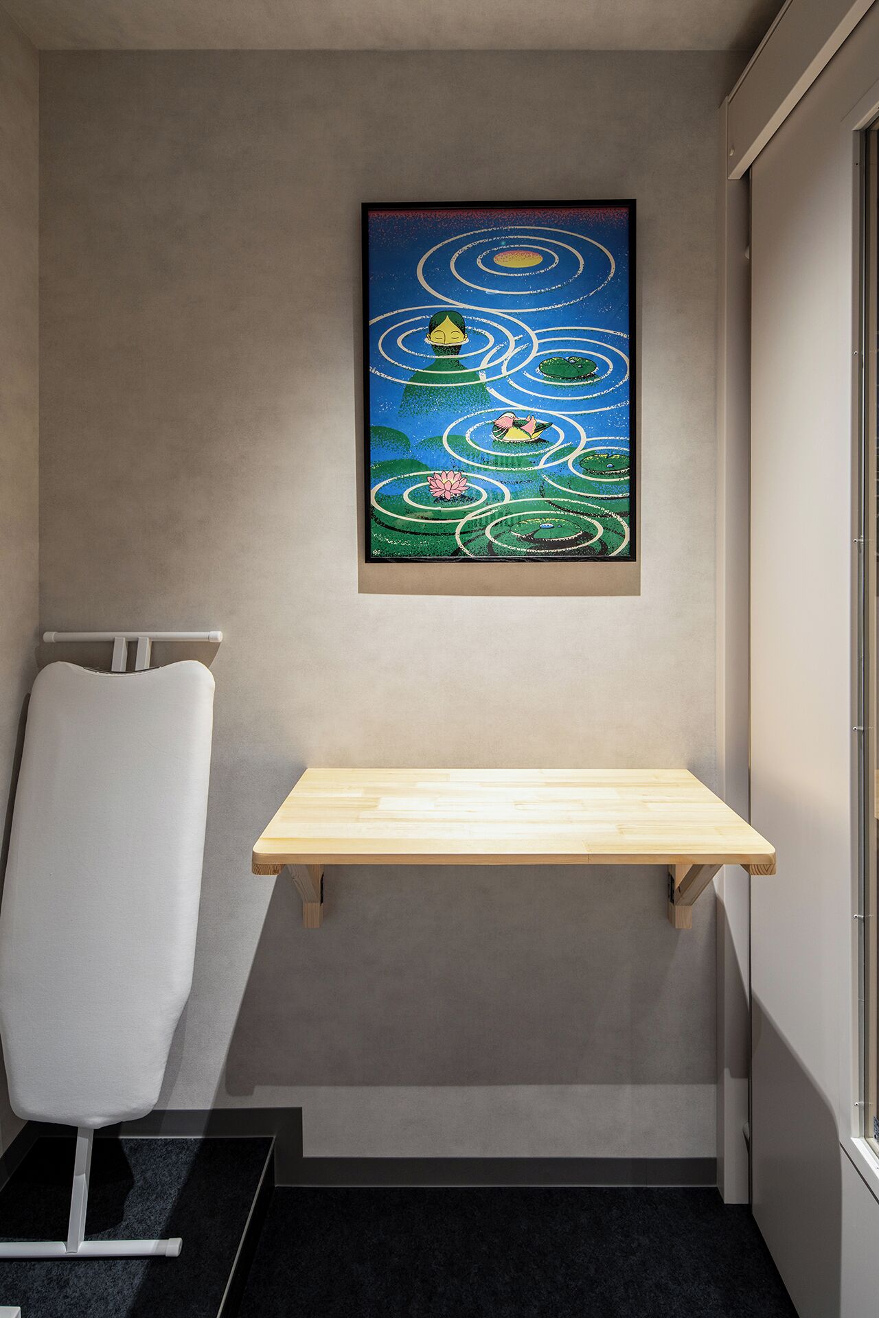 A small room with a wooden shelf, a radiator, and a framed artwork on the wall.