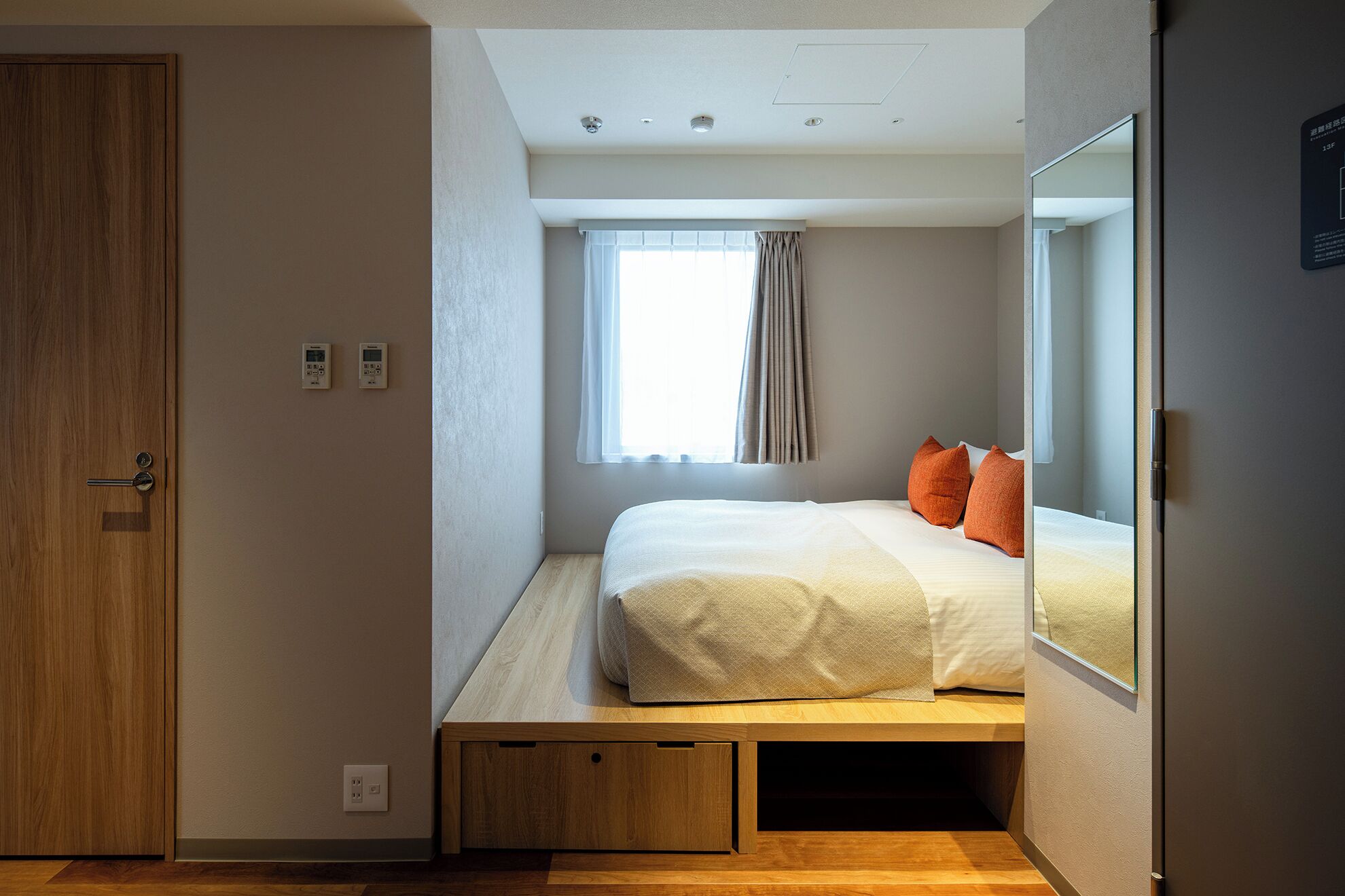 Une chambre à coucher de taille modeste, comprenant un lit, une fenêtre avec des rideaux, une porte en bois et une petite table de chevet.