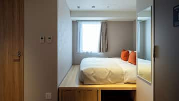 Une chambre à coucher de taille modeste, comprenant un lit, une fenêtre avec des rideaux, une porte en bois et une petite table de chevet.