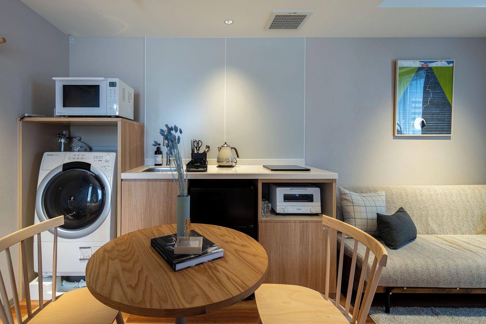 Un espacio habitable compacto con lavadora, microondas, una mesita con un libro y un sofá.
