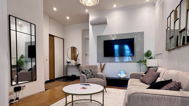 Uma sala de estar moderna com uma mesa de centro redonda, um sofá e uma TV fixada na parede.