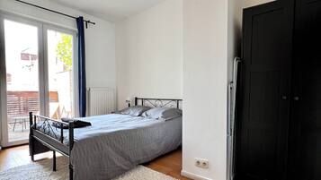Un dormitorio con cama, alfombra blanca, suelo de madera, armario negro y puerta corredera de cristal al exterior.