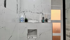 Casa de banho com paredes de mármore, uma pequena prateleira com produtos de higiene pessoal e um espelho.