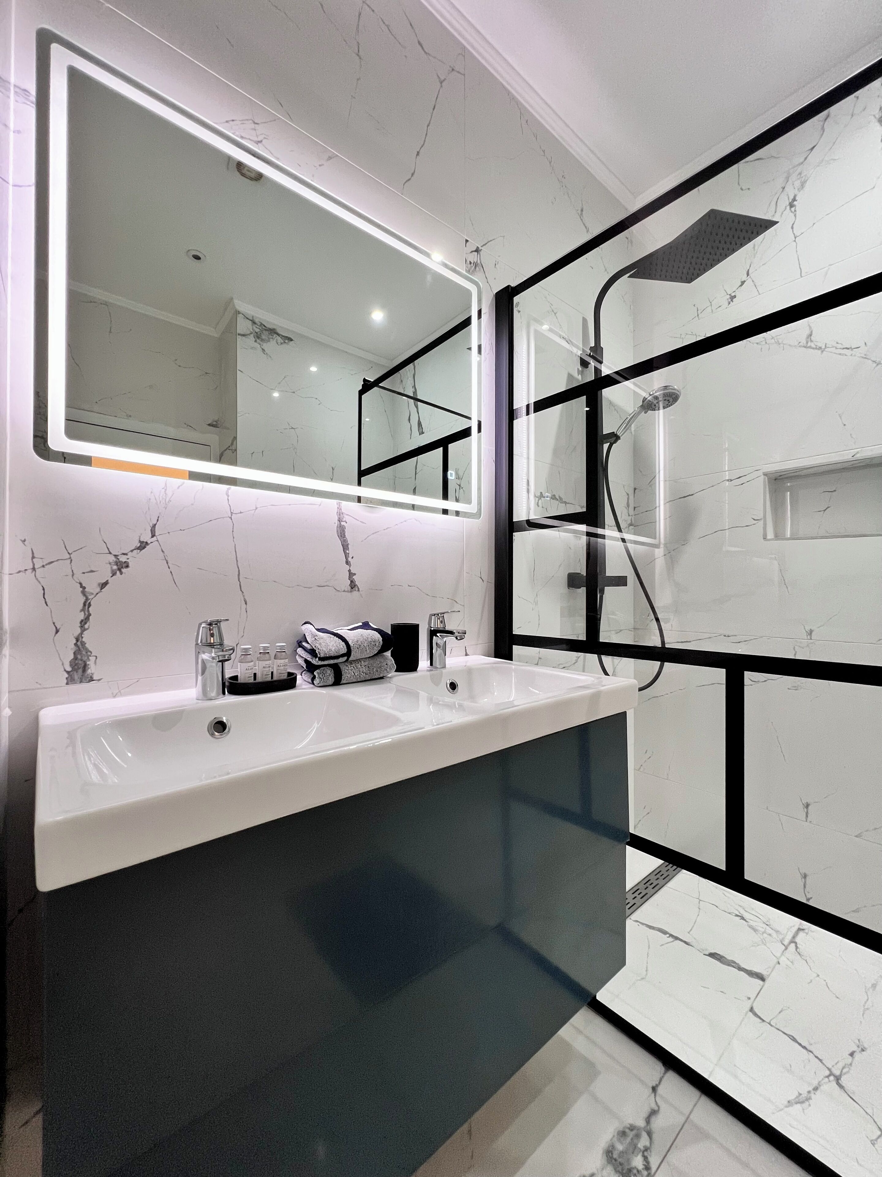 Un bagno moderno con uno specchio grande, due lavandini e una zona doccia.