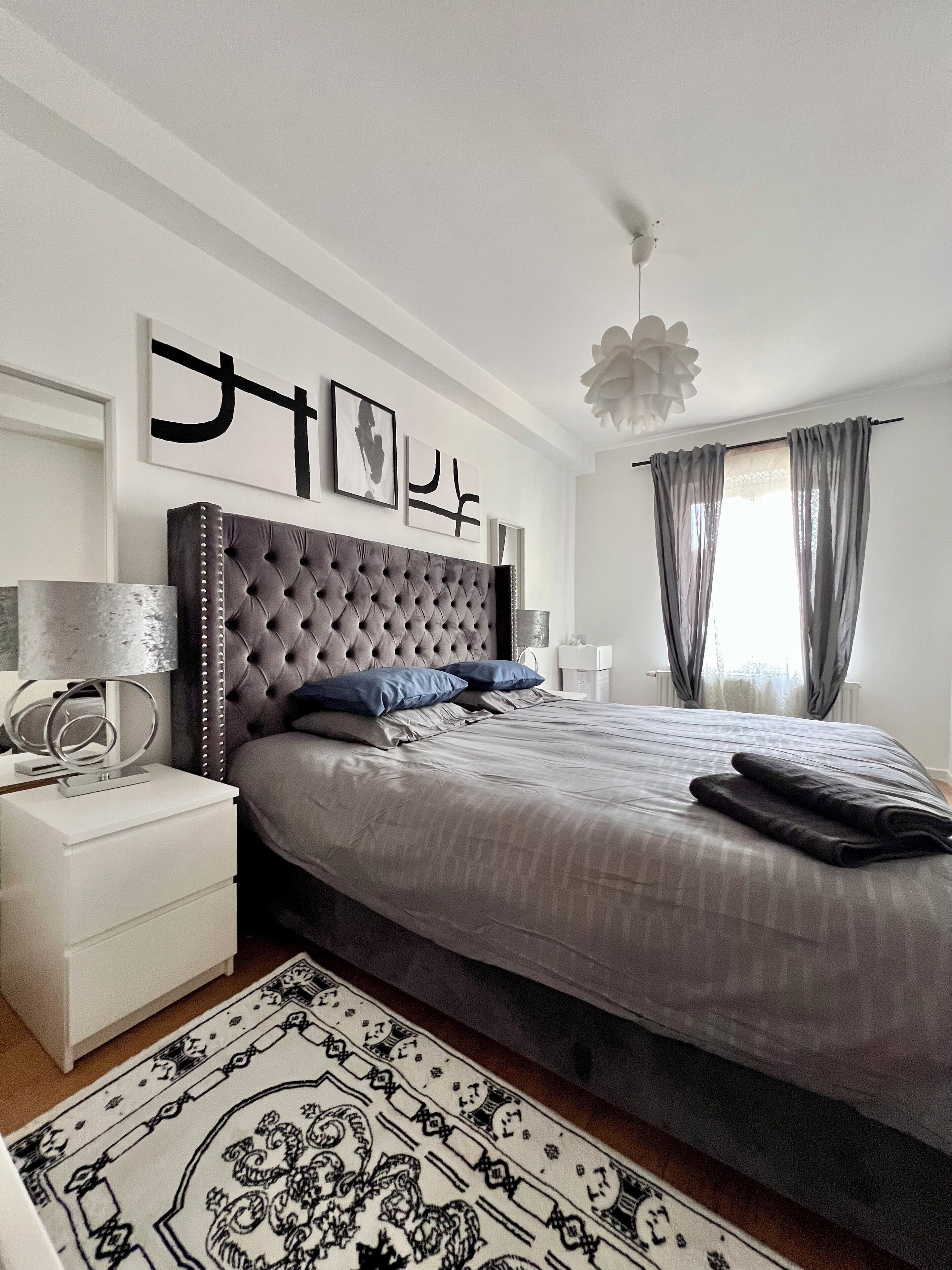 A modern bedroom with a tufted headboard, a large bed, a bedside table with a lamp, and a decorative rug.