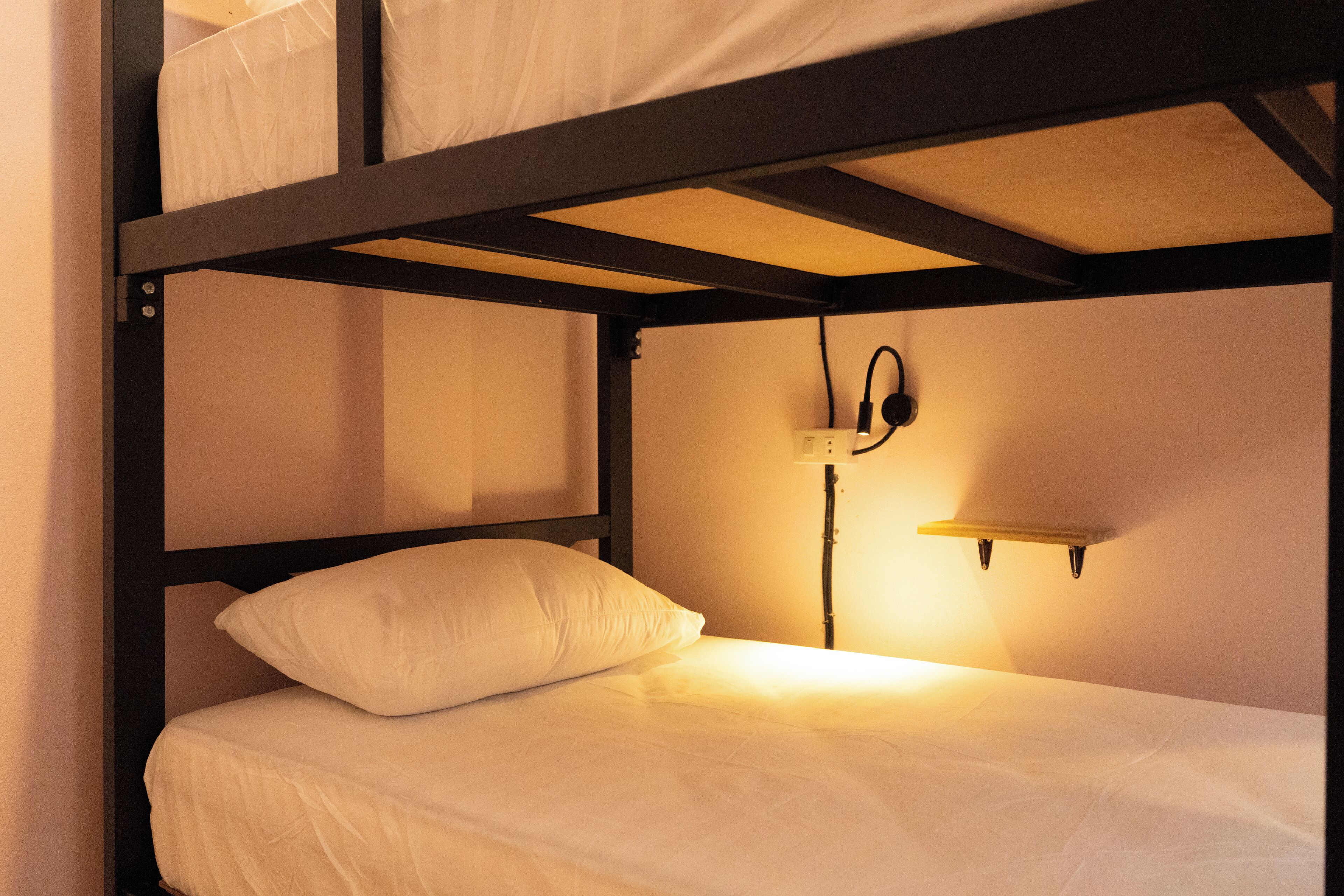 Una cama individual con un único cojín blanco y una mesita de noche con una lámpara.