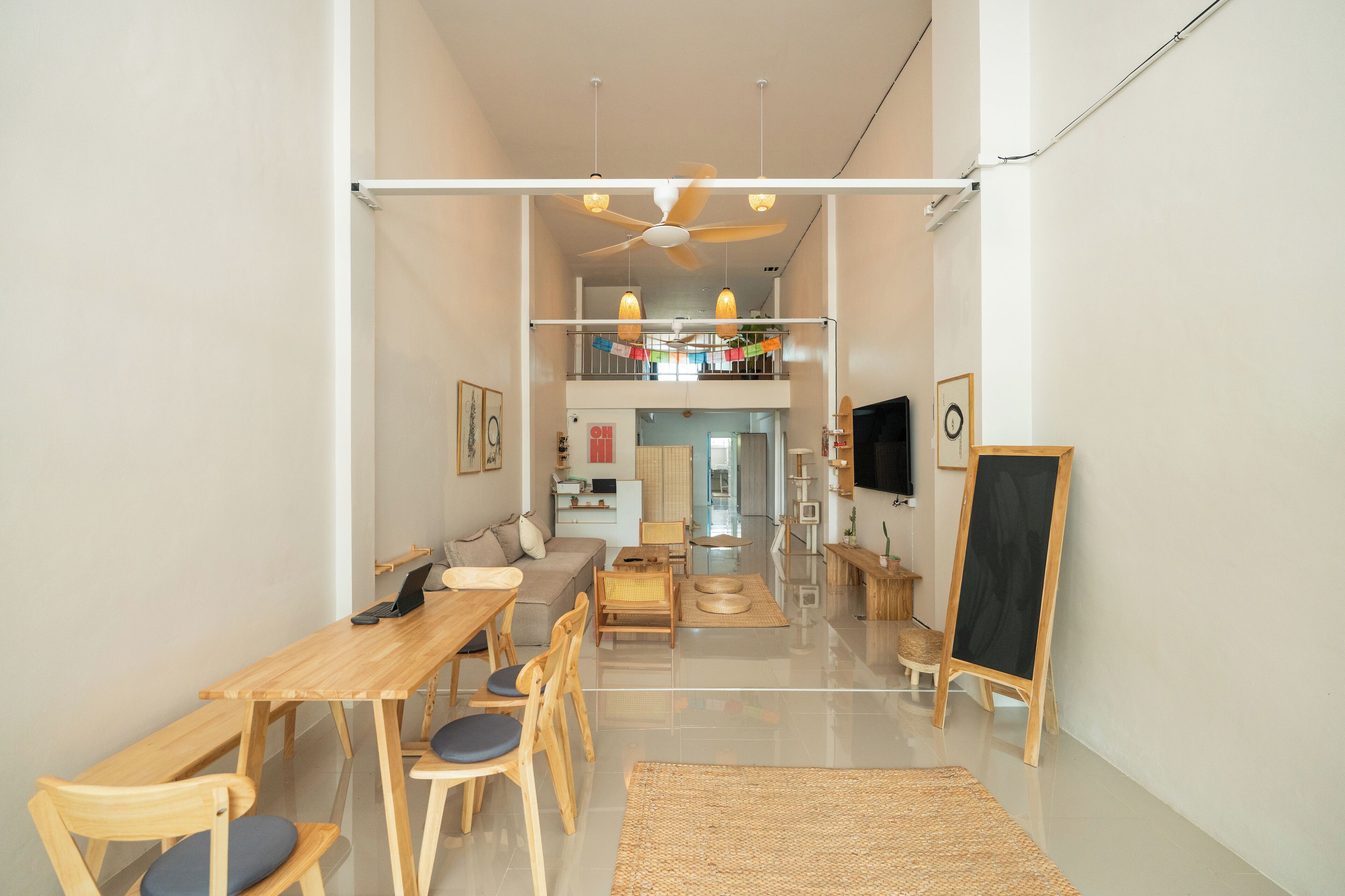Un salón espacioso con una mesa y sillas de madera, un sofá, un ventilador de techo y una pizarra.