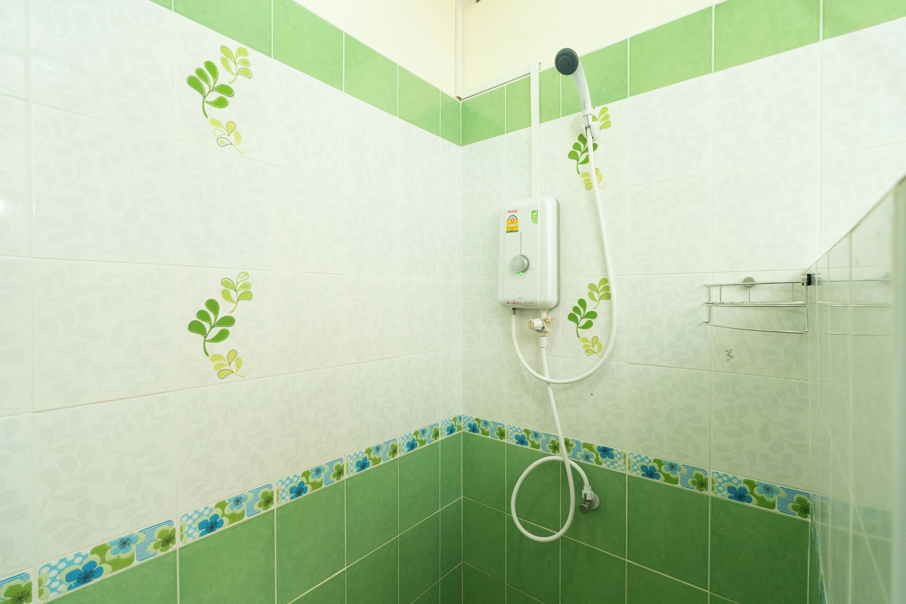 Un baño con azulejos verdes y blancos, una ducha con manguera y dispensador de jabón.