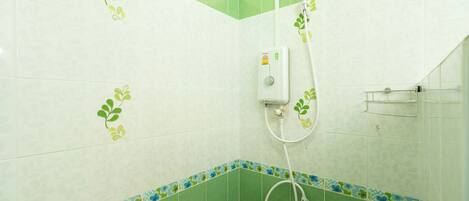 Un baño con azulejos verdes y blancos, una ducha con manguera y dispensador de jabón.